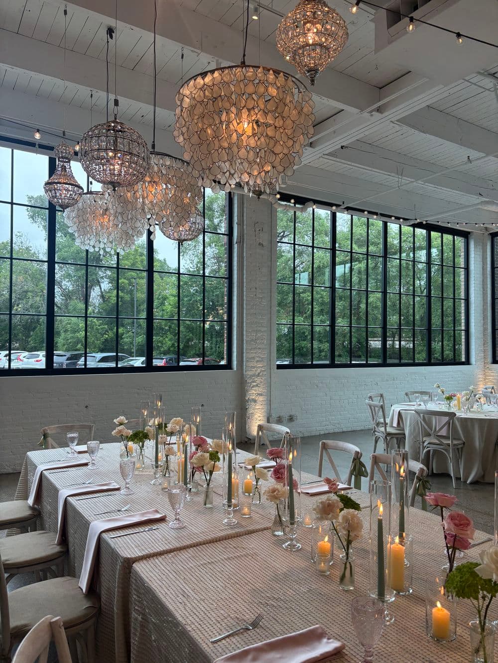 Elegant wedding reception setup with floral centerpieces and crystal chandeliers in a bright venue.